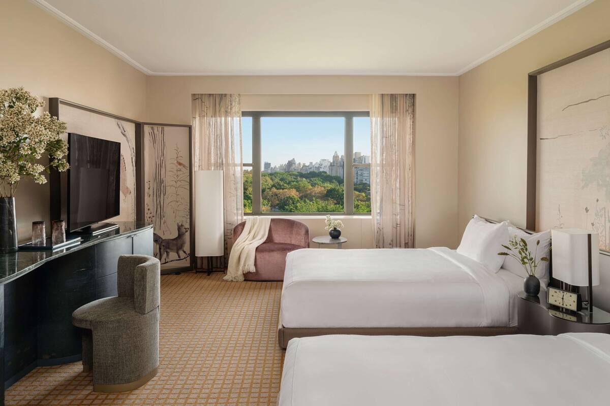 A hotel room with two beds, a TV, a desk, and a view of a cityscape.