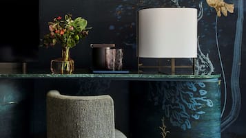 Una habitación moderna con un mural de tonos oscuros, un televisor, un florero con flores, una lámpara y una silla.