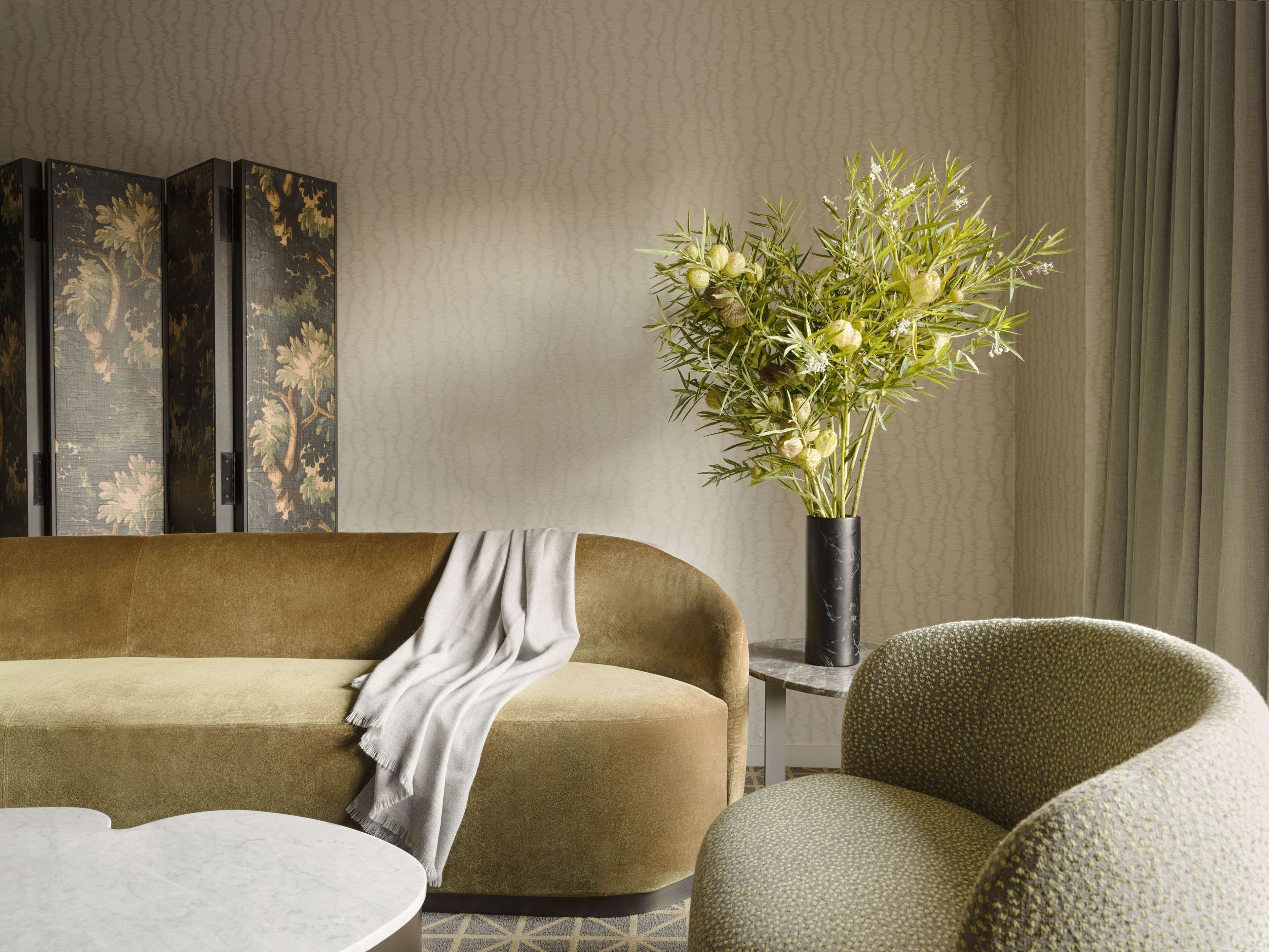 A living room with a sofa, a side table, a vase with flowers, and a patterned wall.