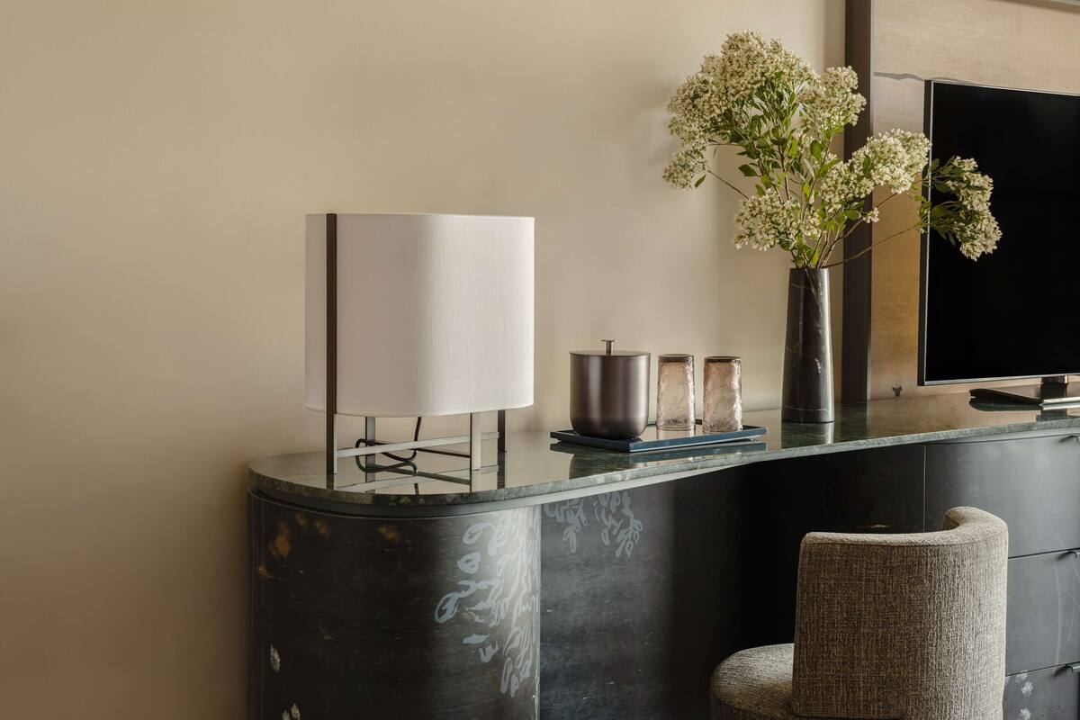 A modern interior with a dark marble counter, a white lamp, a vase with flowers, and a flat-screen TV.