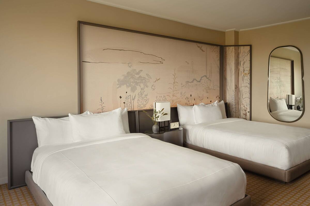 A hotel room with two beds, a large wall mural, a mirror, and a bedside table with a lamp.