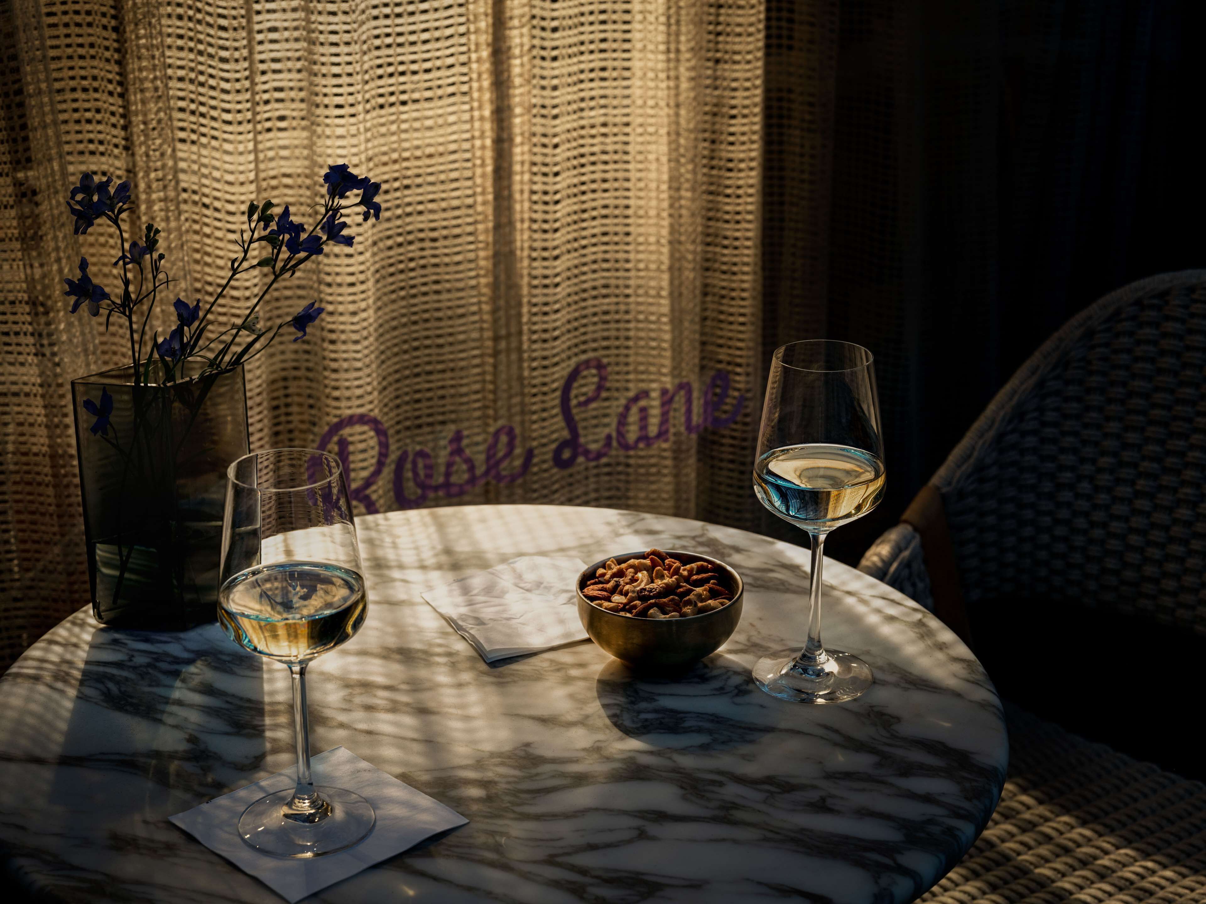 A table with two wine glasses, a bowl of nuts, and a vase of flowers.