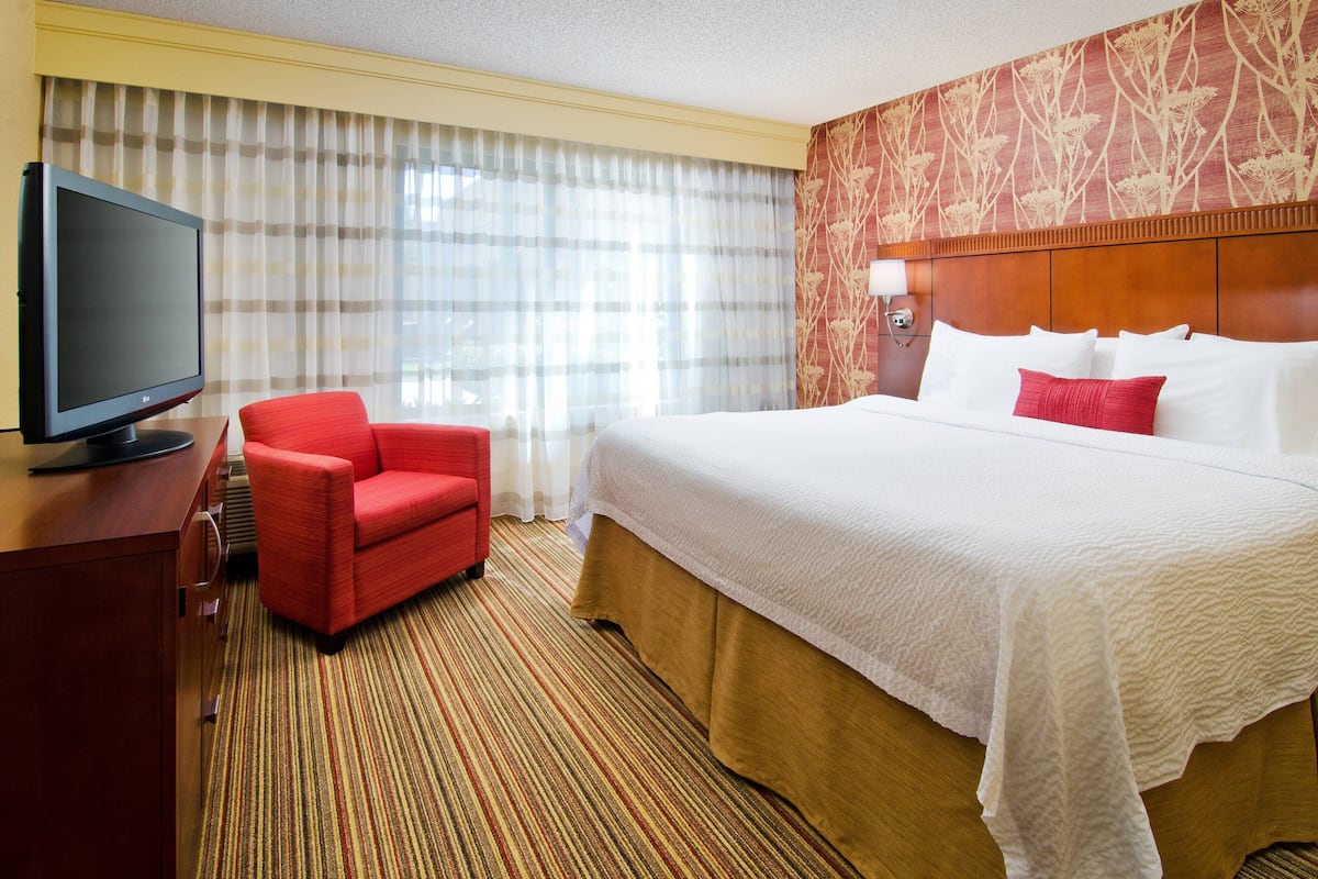 Ein Hotelzimmer mit einem großen Bett, einem roten Sessel, einem Fernseher und einer Wand mit Muster.