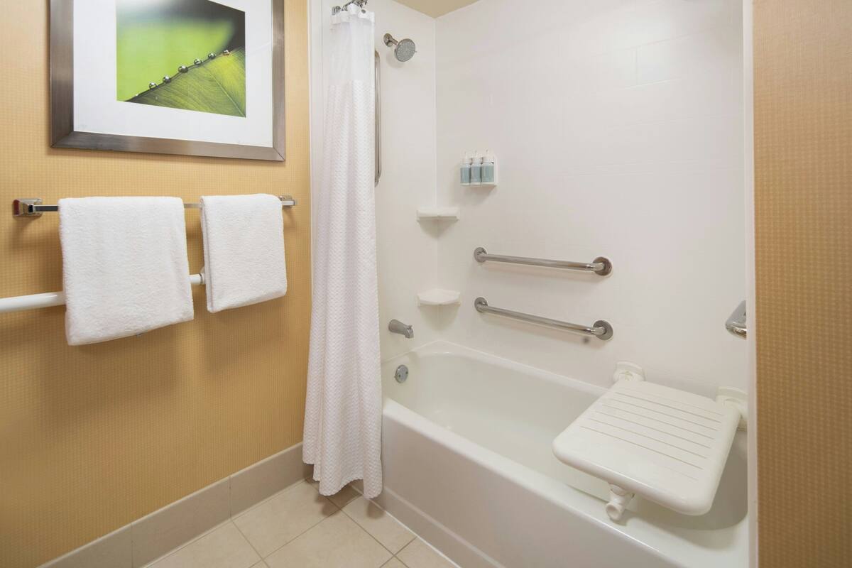 Ein Badezimmer mit einer Badewanne, einer Dusche, einem Handtuchhalter mit zwei Handtüchern und einem gerahmten Bild an der Wand.