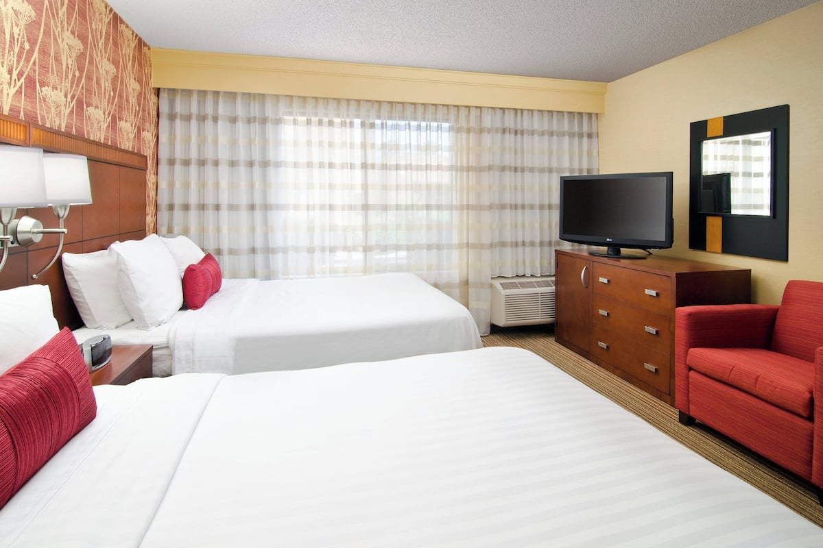Ein Hotelzimmer mit zwei Betten, einem Fernseher, einem roten Sessel und einer Holzkommode.