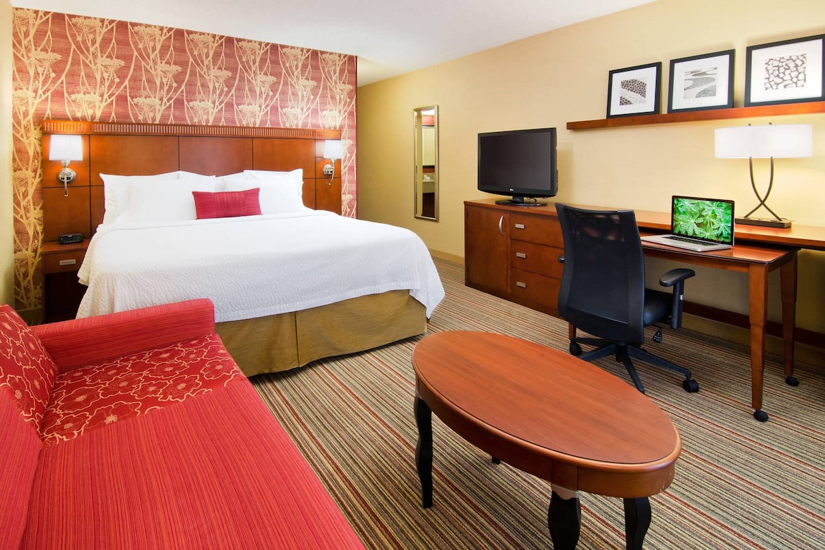 Ein Hotelzimmer mit Bett, Schreibtisch mit Computer, Stuhl, Fernseher und einem roten Sofa.
