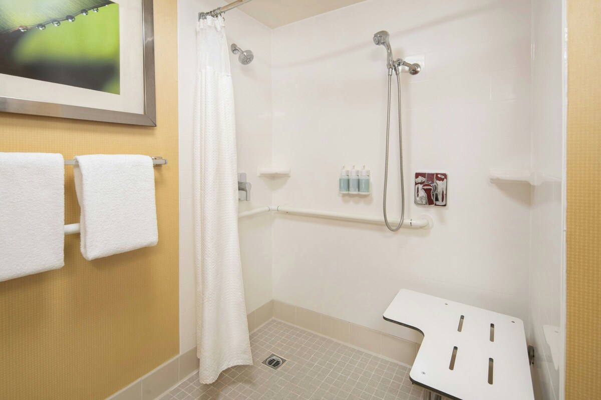 Un baño con ducha, un perchero con dos toallas, una cortina de ducha y un pequeño estante con artículos de aseo.