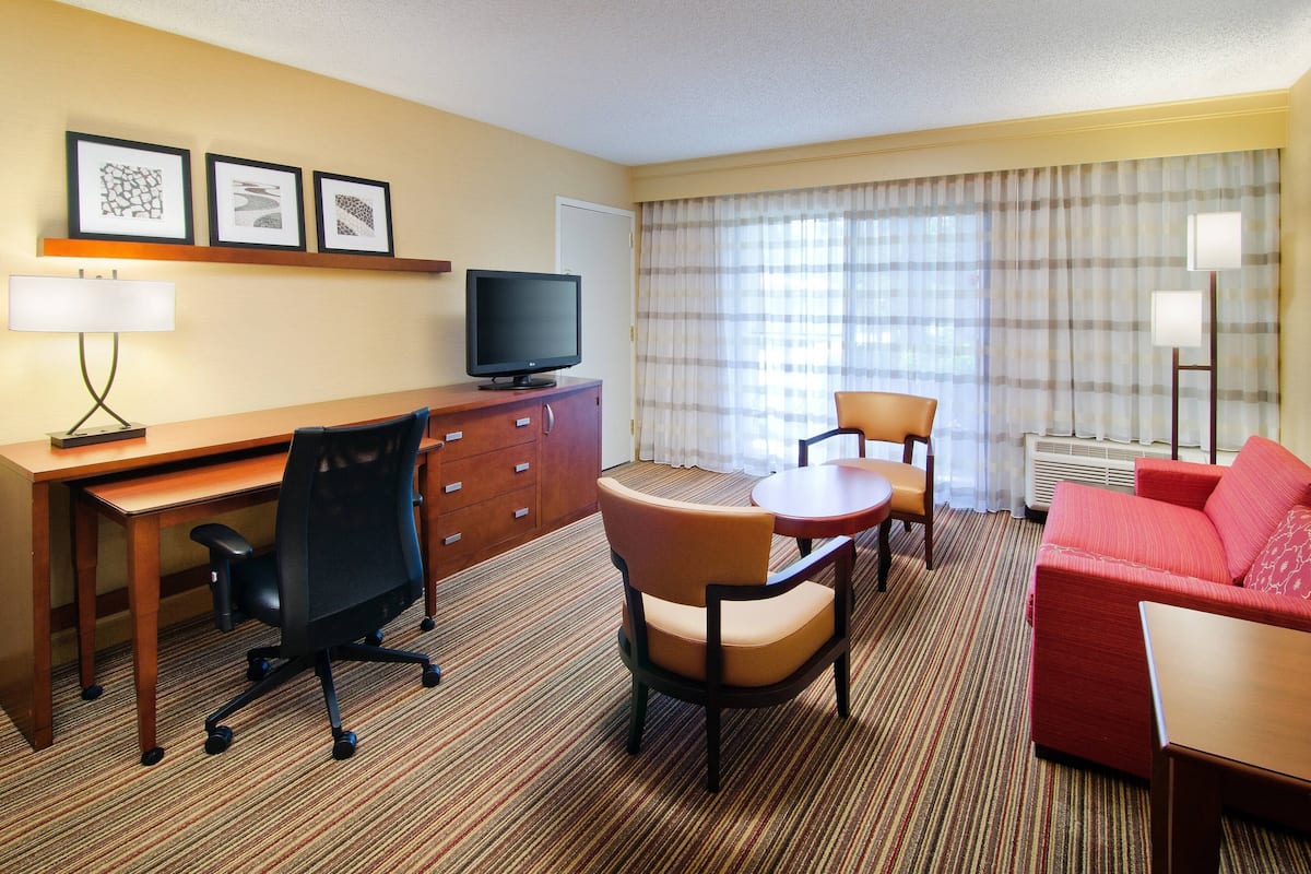 Ein Hotelzimmer mit Schreibtisch aus Holz, einem Fernseher, einem roten Sofa und einem kleinen Esstisch.