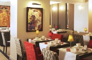 A restaurant with tables set for dining, chairs with patterned covers, and a painting on the wall. - Hotel Eiffel Seine (Paris)