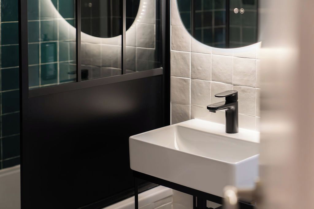 Une salle de bain moderne avec un lavabo blanc, un robinet noir et des murs recouverts de carreaux foncés.