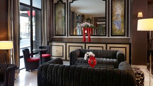 A hotel lobby with a large window, a red vase with flowers, and a black sofa. - Hotel Eiffel Seine (Paris)