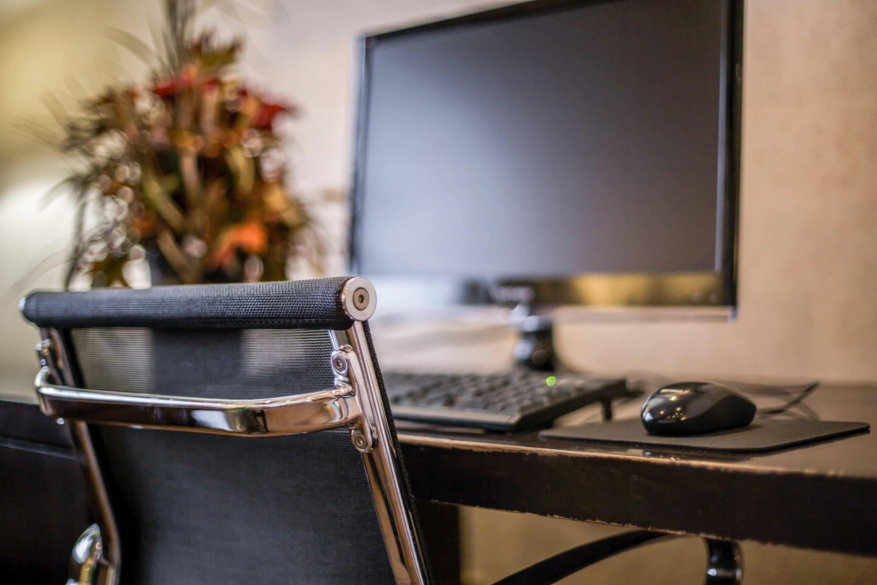 A chair with a metal frame and a black seat, a computer monitor, a keyboard, and a mouse on a desk.