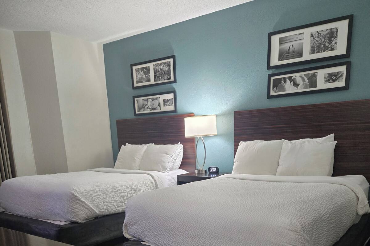 A hotel room with two beds, a nightstand with a lamp, and framed pictures on the wall.