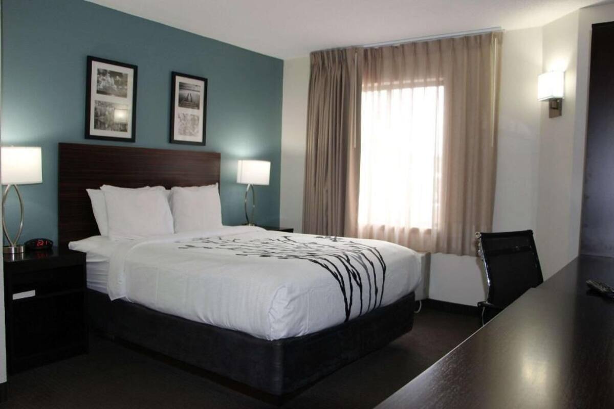A hotel room with a bed, bedside lamps, a desk, and a window with curtains.