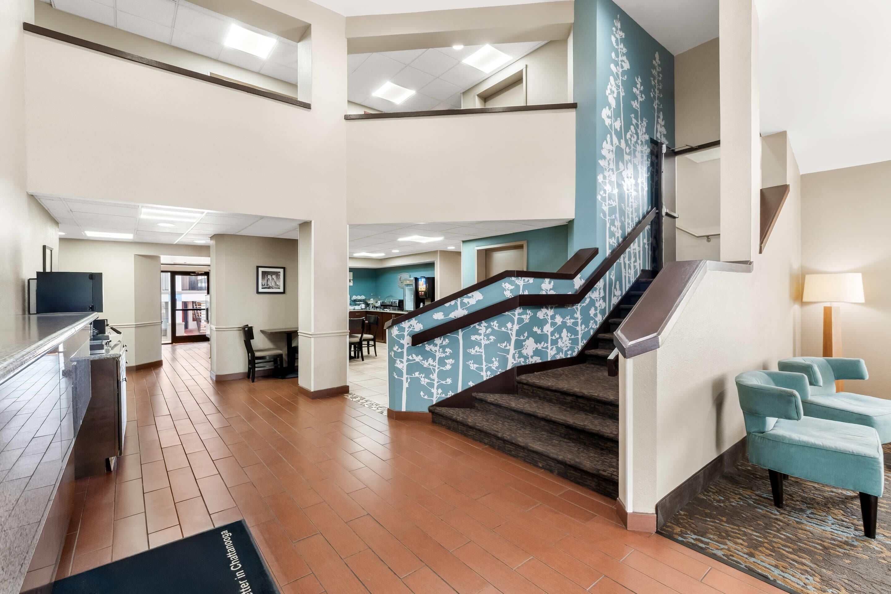 A hotel lobby with a staircase, a reception desk, and a dining area.