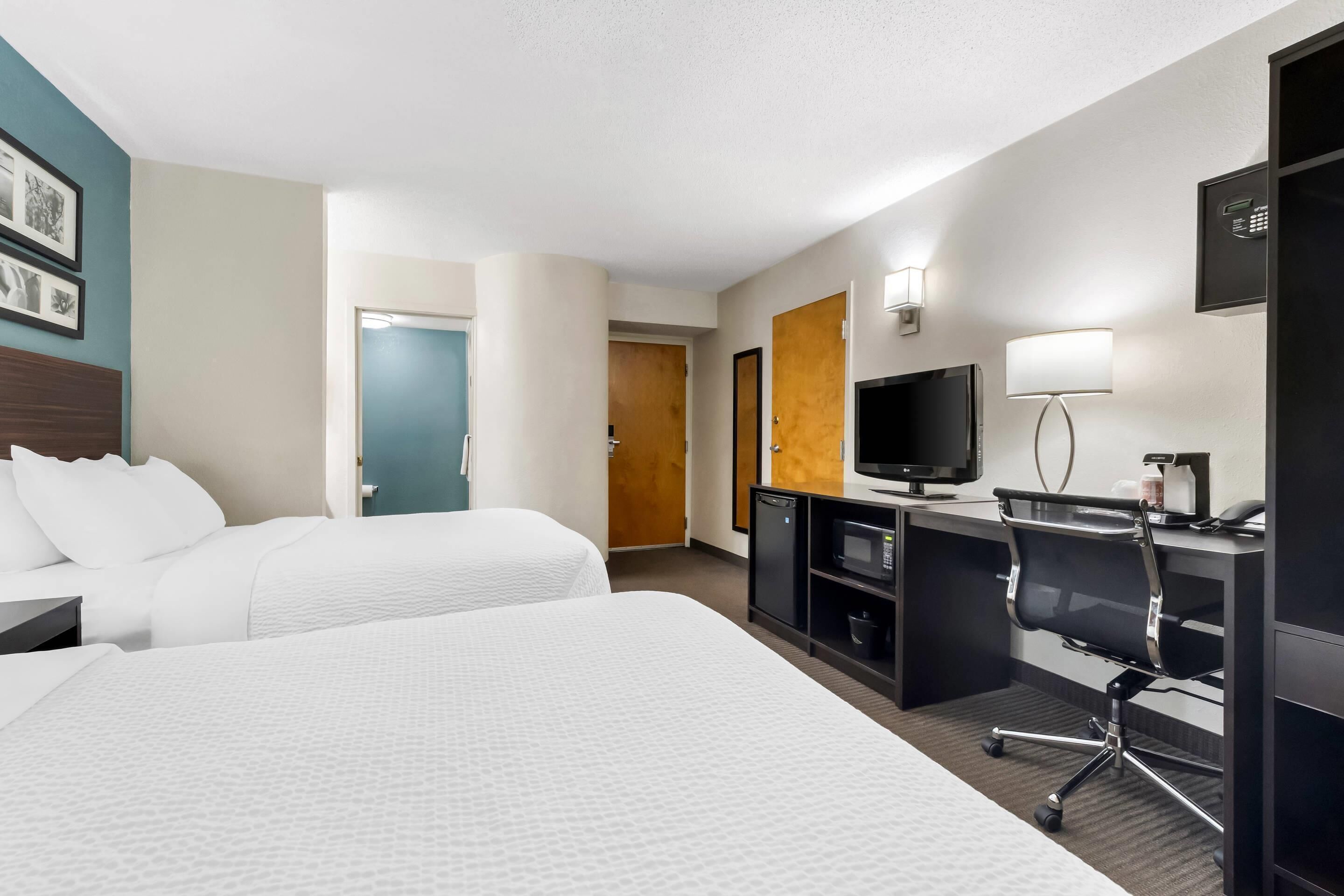 Ein Hotelzimmer mit zwei Betten, einem Schreibtisch mit Computer, einem Fernseher und einer Minibar.