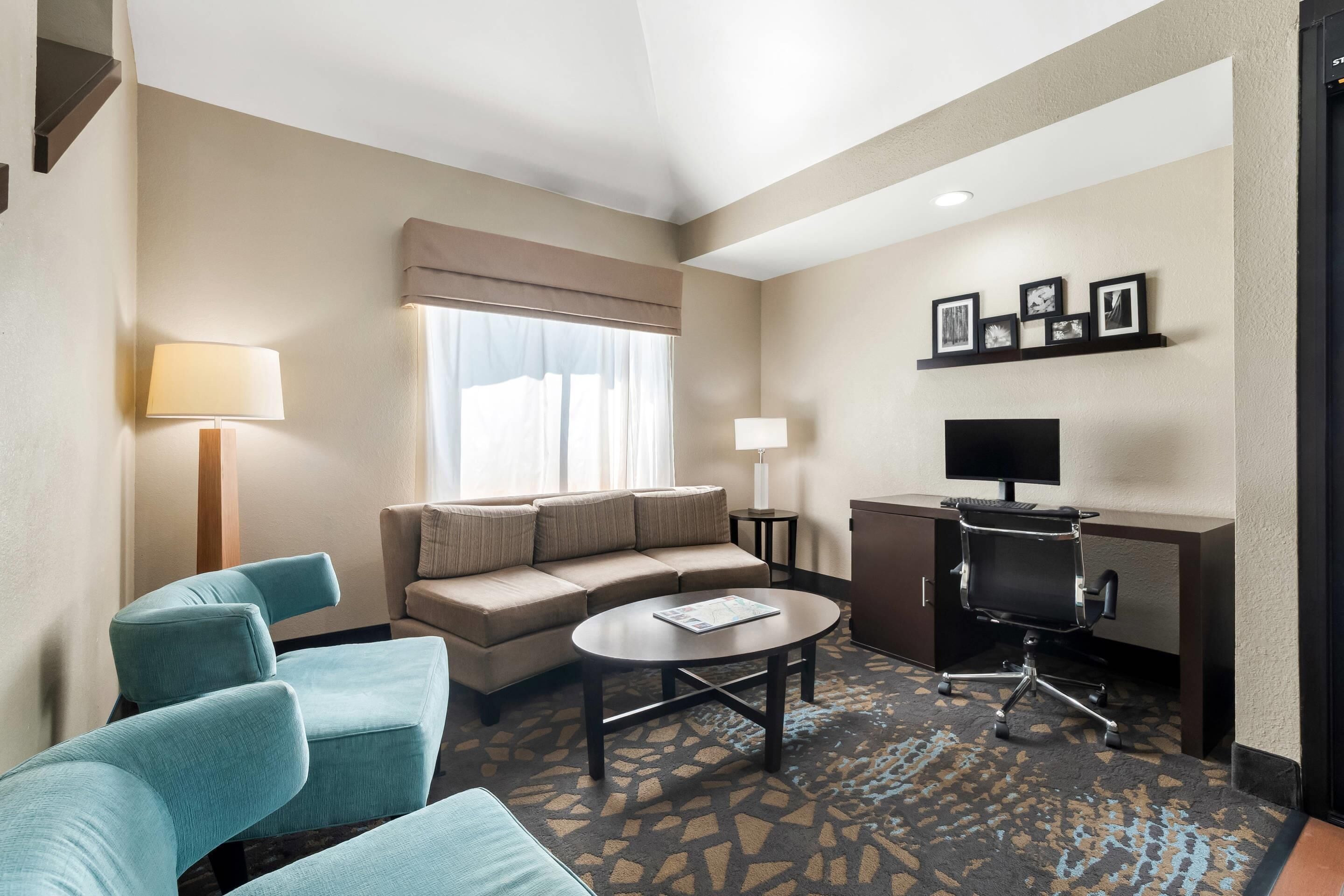 Habitación de hotel con sofá, dos sillones, una mesa de centro, un escritorio con computadora y televisión.