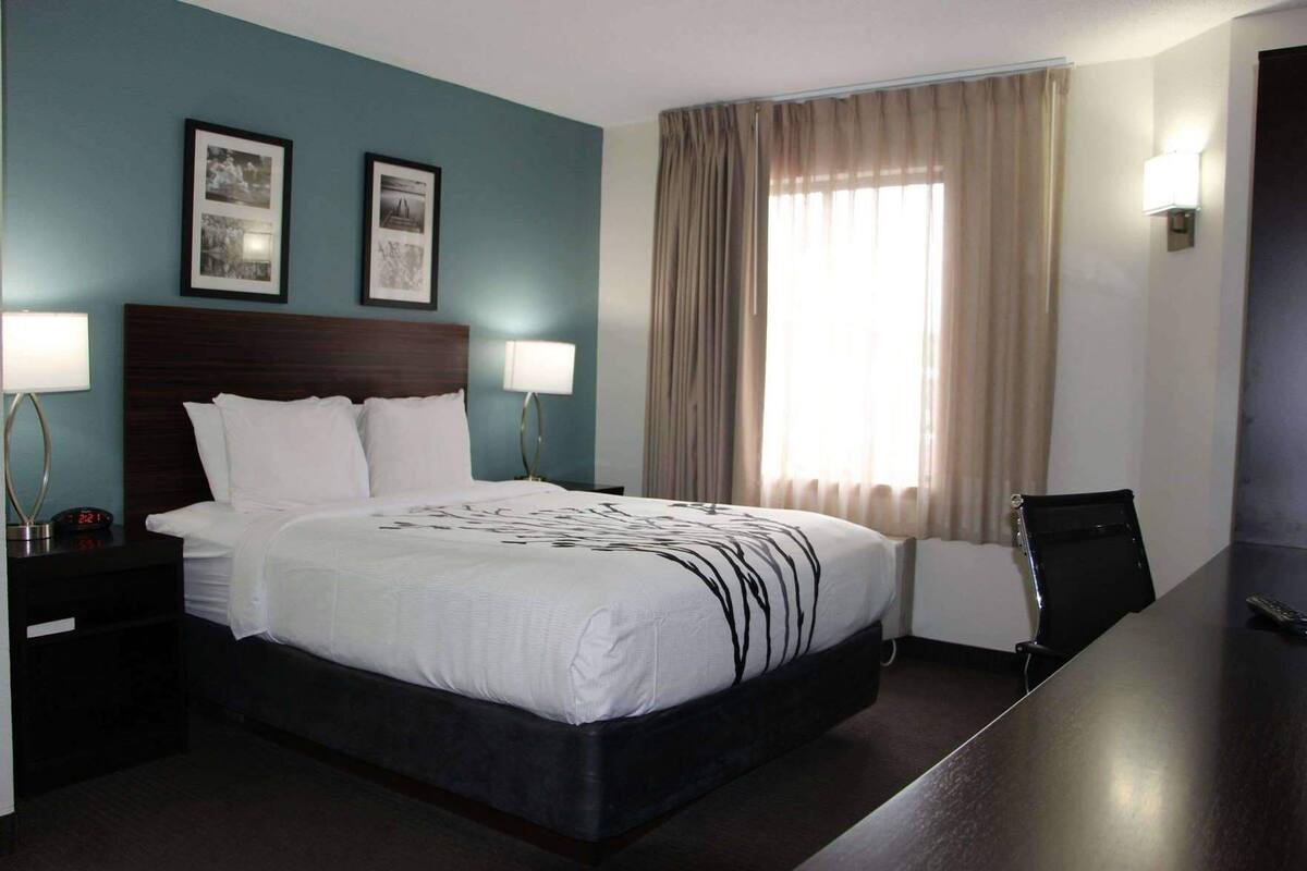 A hotel room with a bed, two bedside lamps, a desk, and a chair.