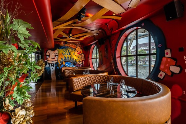 A restaurant with round tables and cushioned booths, large windows, and a mural on the wall.