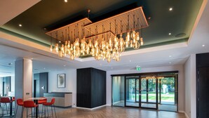 A spacious lobby with a modern chandelier, a reception desk, and a view of the outdoors. - Holiday Inn London - Shepperton by IHG (Shepperton)