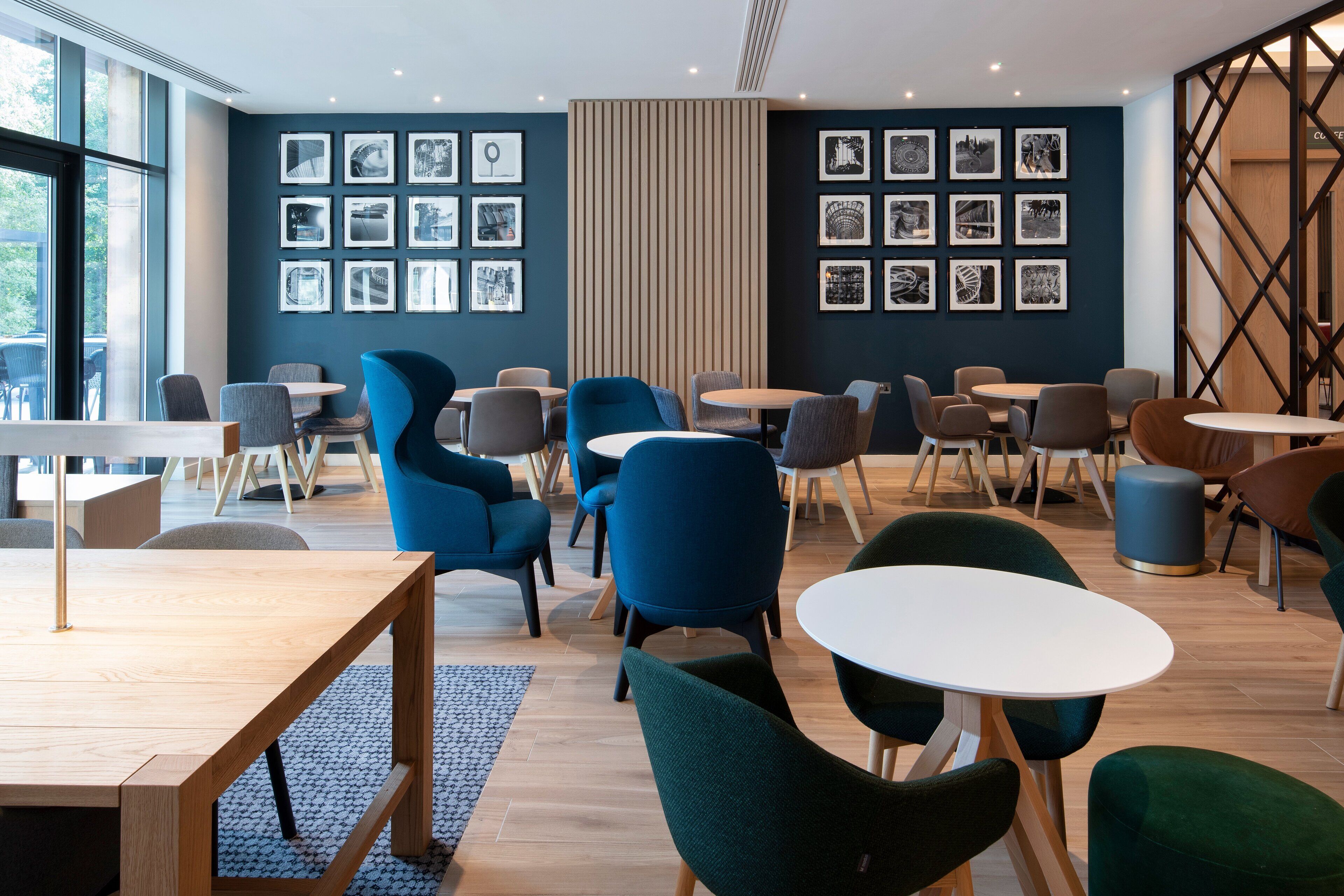 Ein modernes Café mit Holztischen und -stühlen, einem großen Fenster und Schwarzweißfotos an den Wänden.