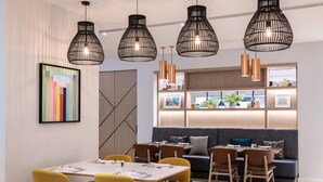 A modern dining area with a long table, yellow chairs, and black pendant lights. - Holiday Inn London - Shepperton by IHG (Shepperton)