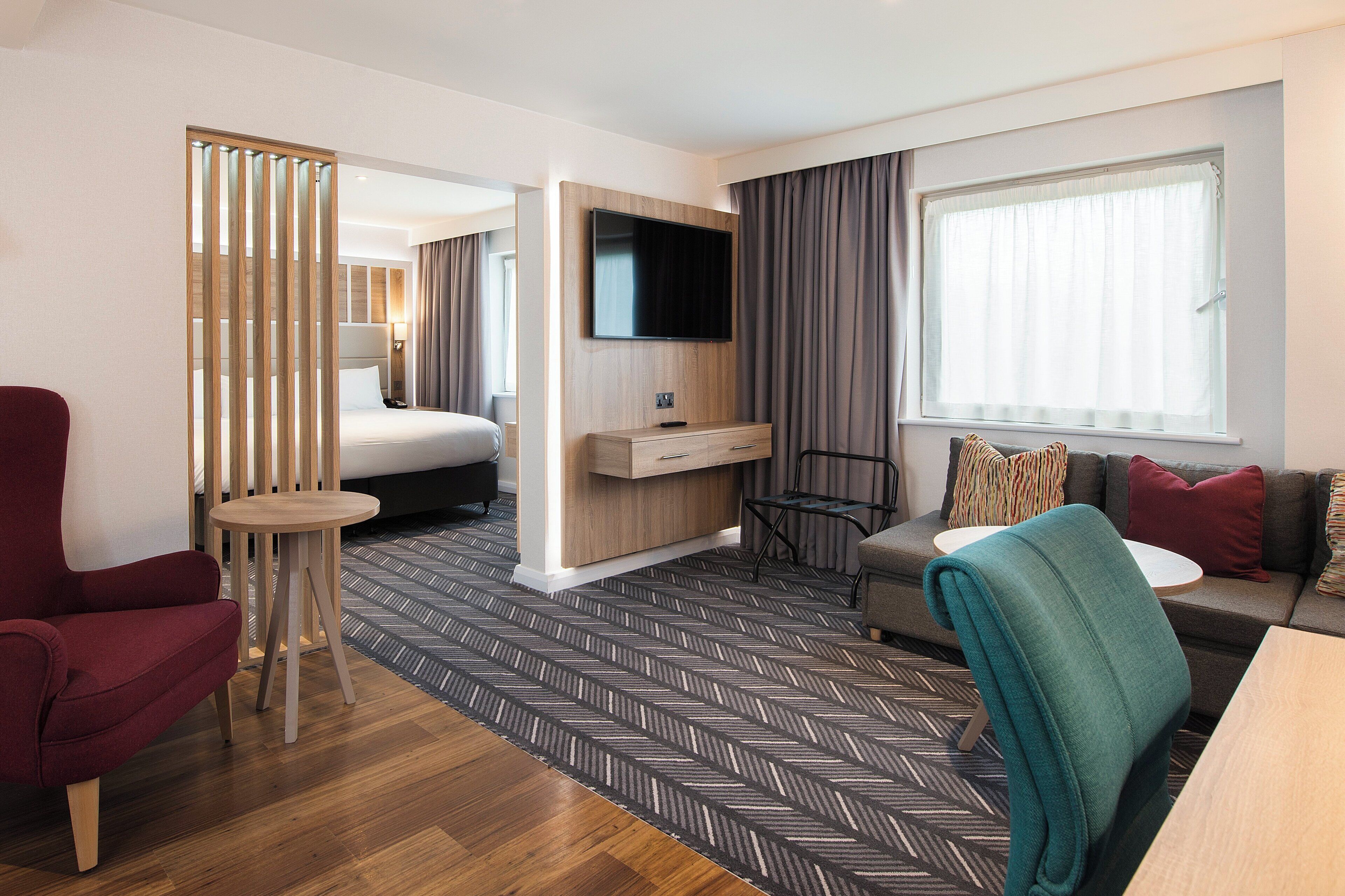Une chambre d’hôtel moderne équipée d’un lit, d’un téléviseur fixé au mur, d’un canapé, d’une petite table et d’une chaise.