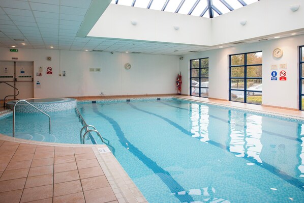 An indoor swimming pool with clear water, tiled floor, and a skylight above.