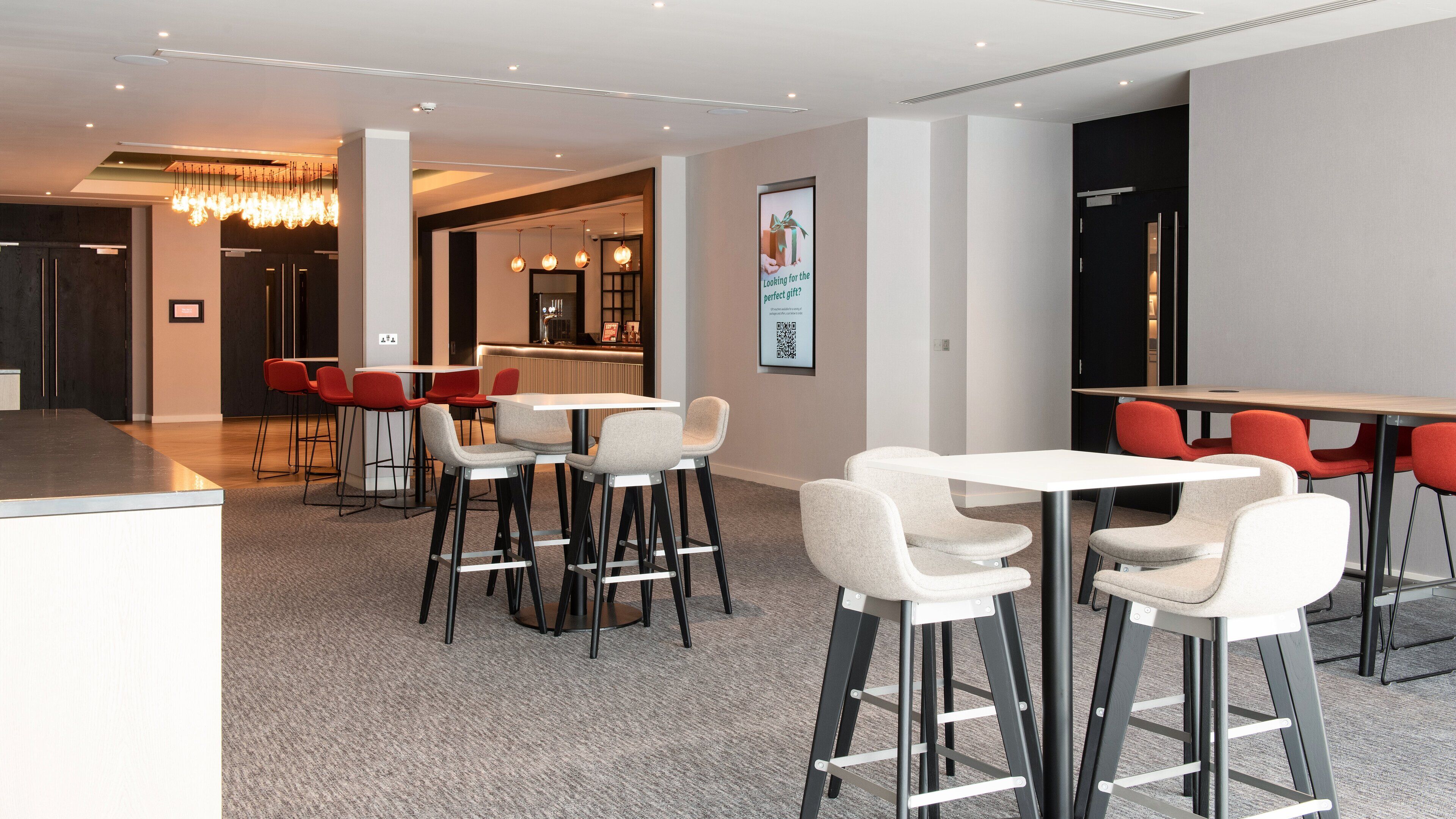 A modern hotel lobby with a reception desk, seating area with bar stools, and a counter.