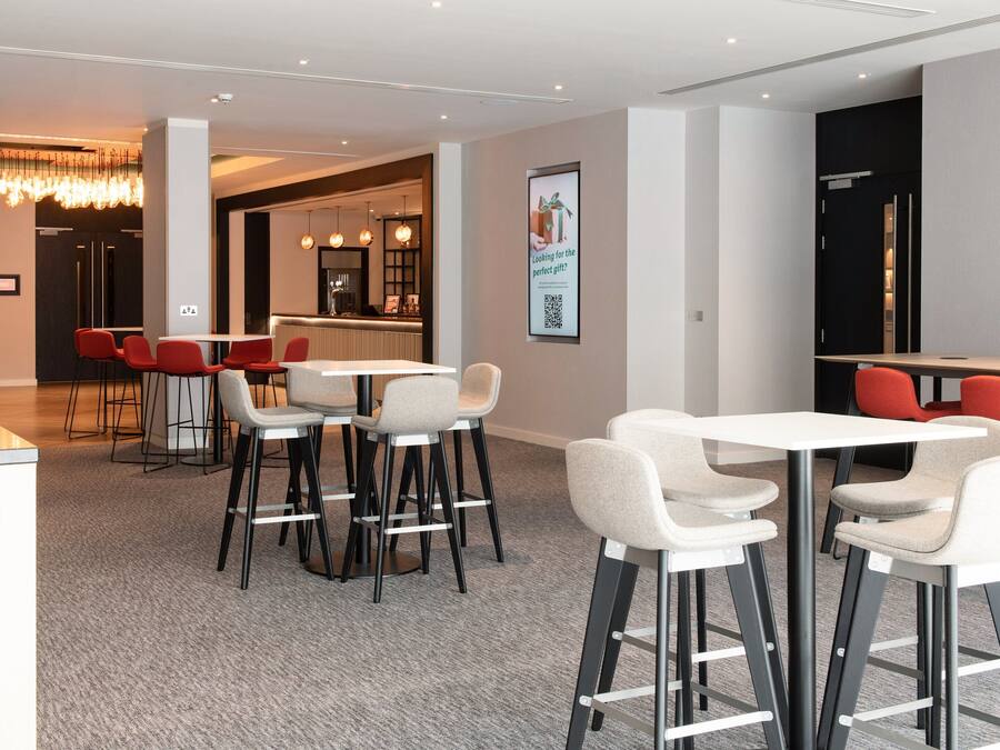 Un moderno vestíbulo de hotel con una recepción, una zona de estar con taburetes de bar y una barra.