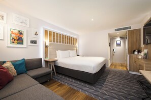A modern hotel room with a large bed, a sofa, a small table, and a TV.