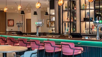 Een bar met roze stoelen, een groene toonbank en een wijnrek.