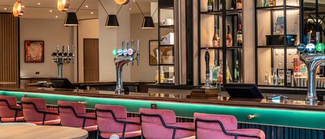 A bar area with pink chairs, a green counter, and a wine display.