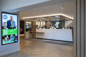 Experience the hotel's modern lobby, featuring a minimalist reception desk, digital screen, and inviting atmosphere.