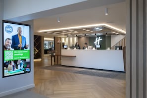 Experience the hotel's modern lobby, featuring a minimalist reception desk, digital screen, and inviting atmosphere.