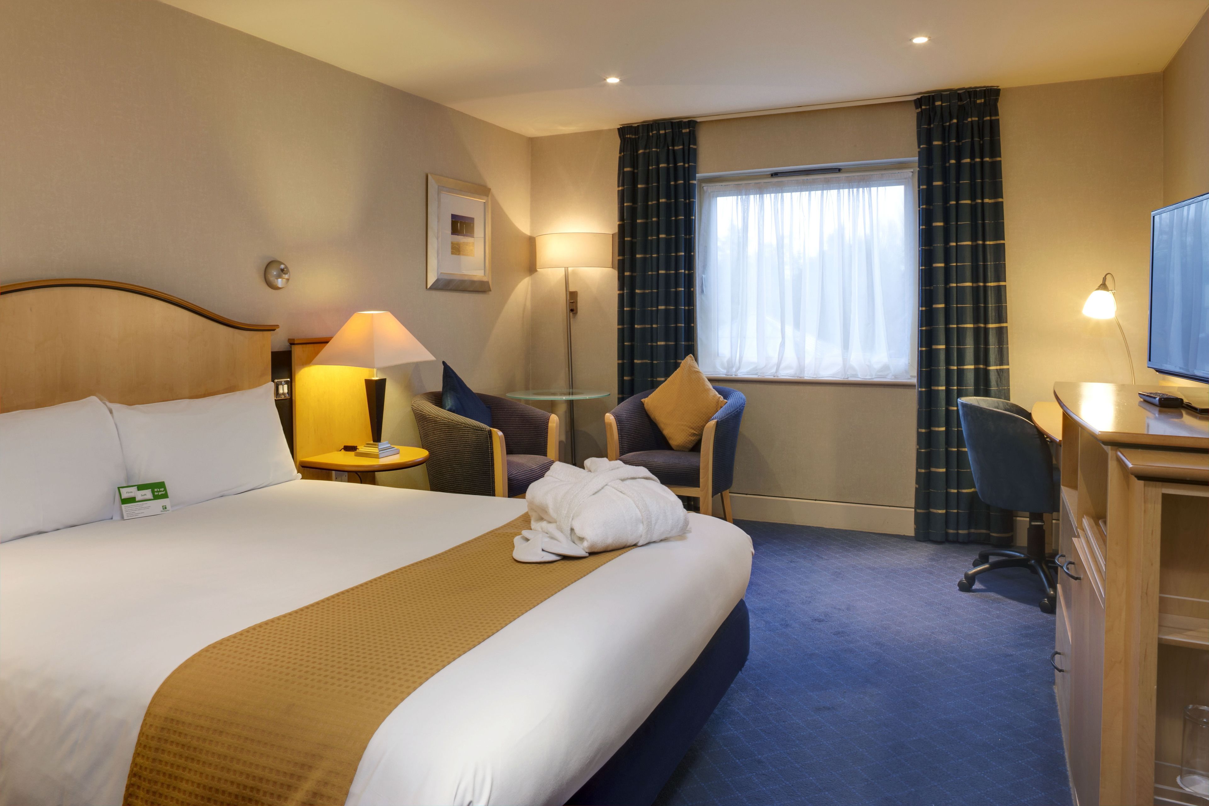 A hotel room with a large bed, a desk, a chair, a lamp, and a television.