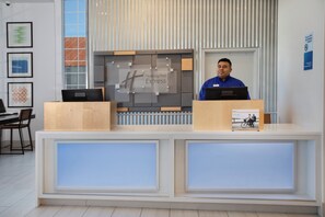 A hotel reception desk with a modern design, a large window, and framed artwork on the wall.
