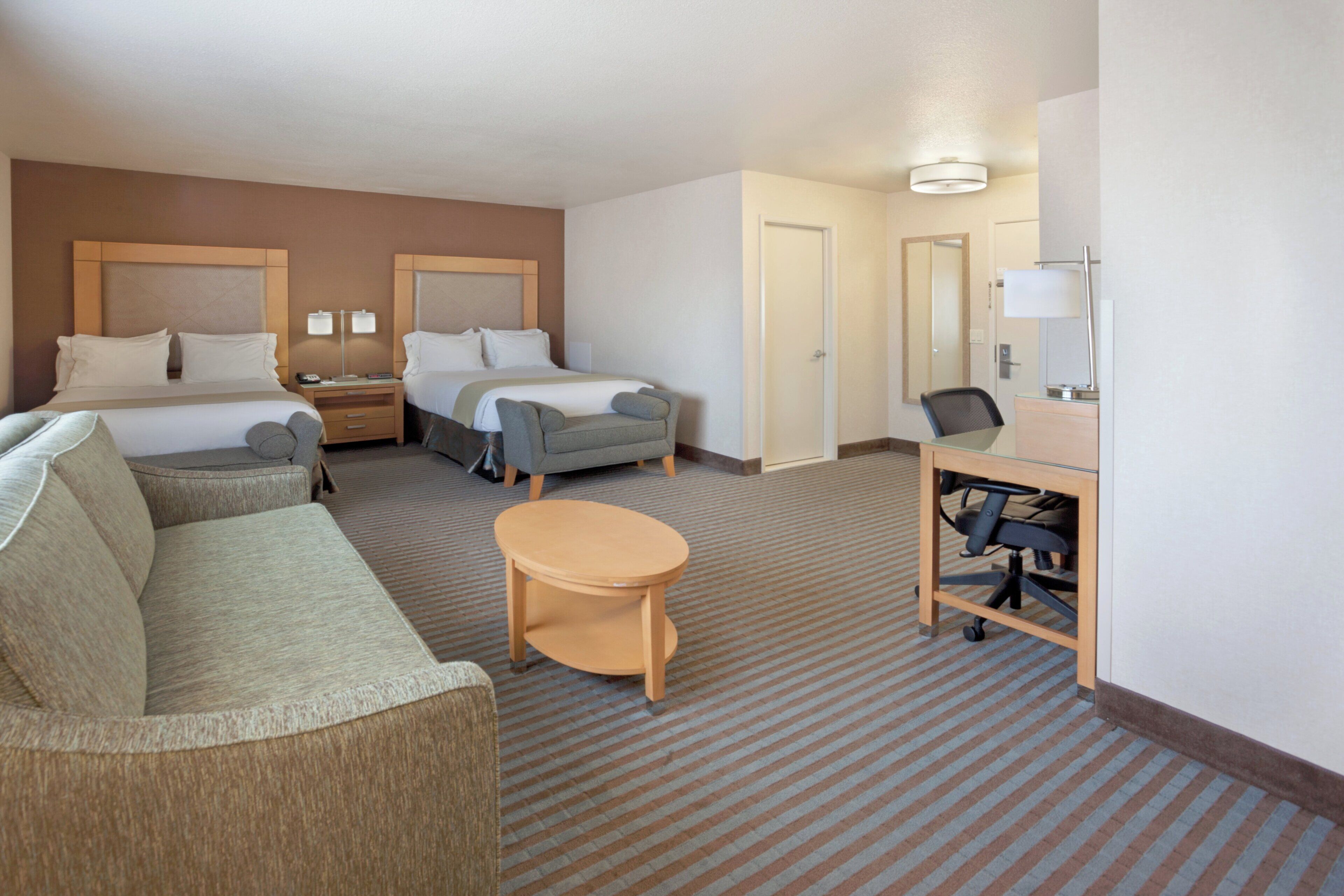 A hotel room with two beds, a sofa, a desk with a chair, and a small table.