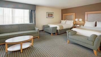 Habitación de hotel con sofá, dos sillones, una mesita, cama y mesita de noche con lámpara.
