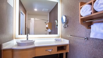 A bathroom with a large mirror, a sink, a towel rack, and a shower area.
