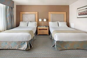 A hotel room with two beds, a nightstand with a lamp, and a framed picture on the wall.