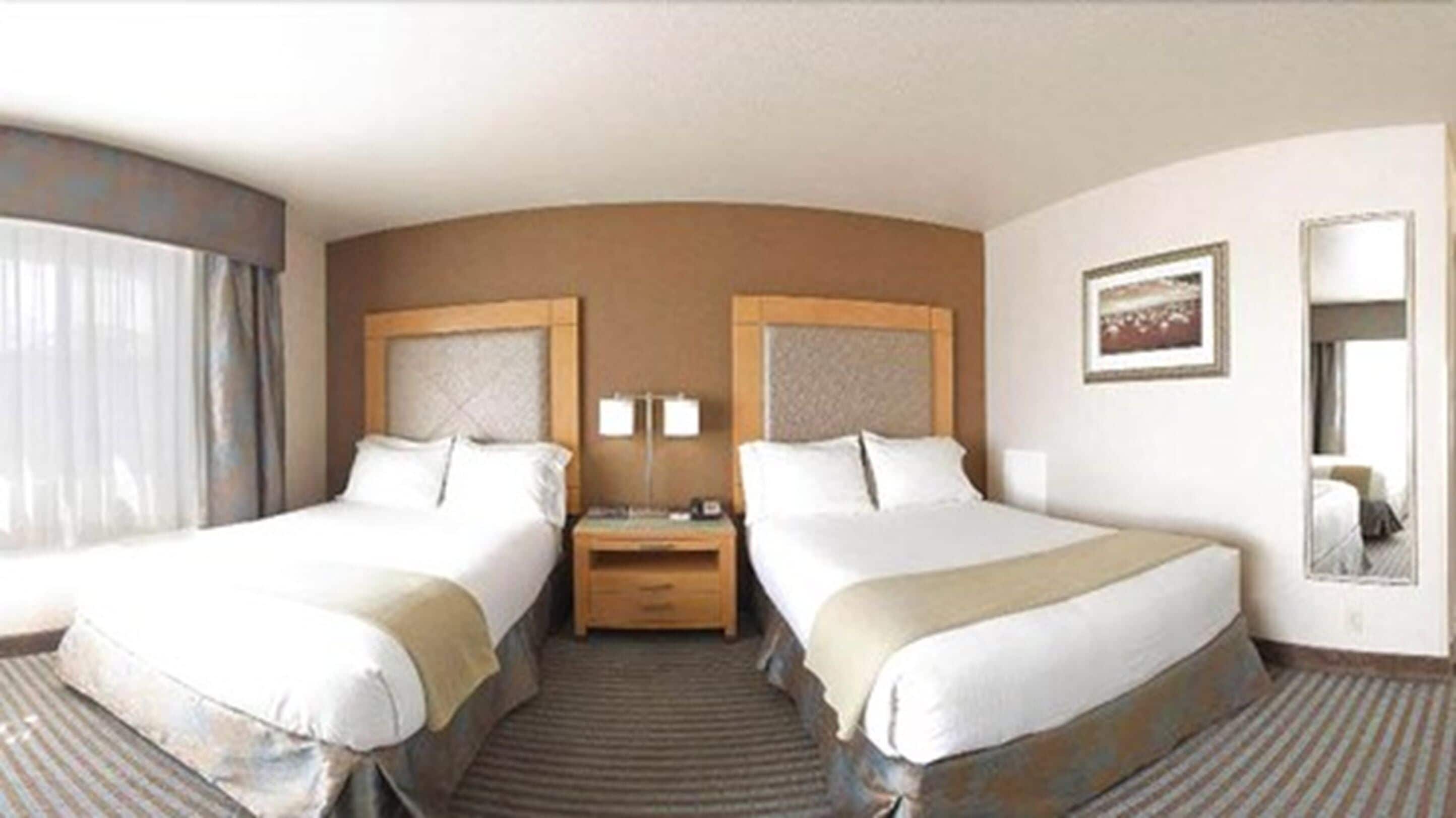 A hotel room with two beds, a nightstand, a lamp, and a painting on the wall.
