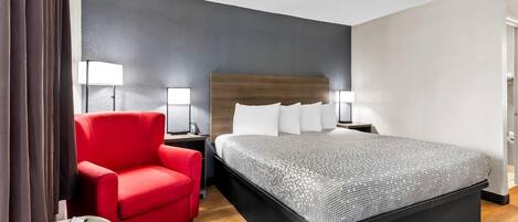 Habitación de hotel con una cama grande, un sillón rojo, dos lámparas de noche y un calentador de pared.