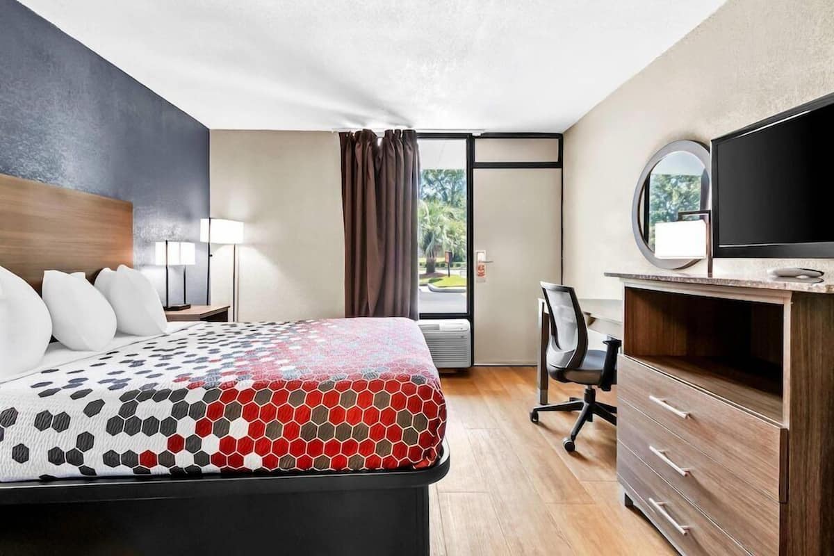 A hotel room with a bed, desk, chair, TV, and a window with curtains.