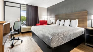 Una habitación de hotel moderna con una cama grande, un escritorio con una silla, un sillón rojo y un ventanal con cortinas.
