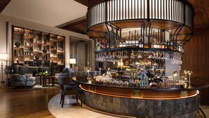 A bar area with a curved counter, shelves with bottles, and a seating area with chairs and a table. - Artyzen Grand Lapa Macau (Macau)