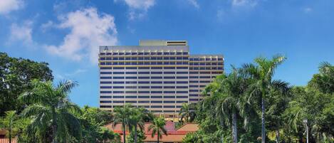A hotel with a large building, a swimming pool, and palm trees.