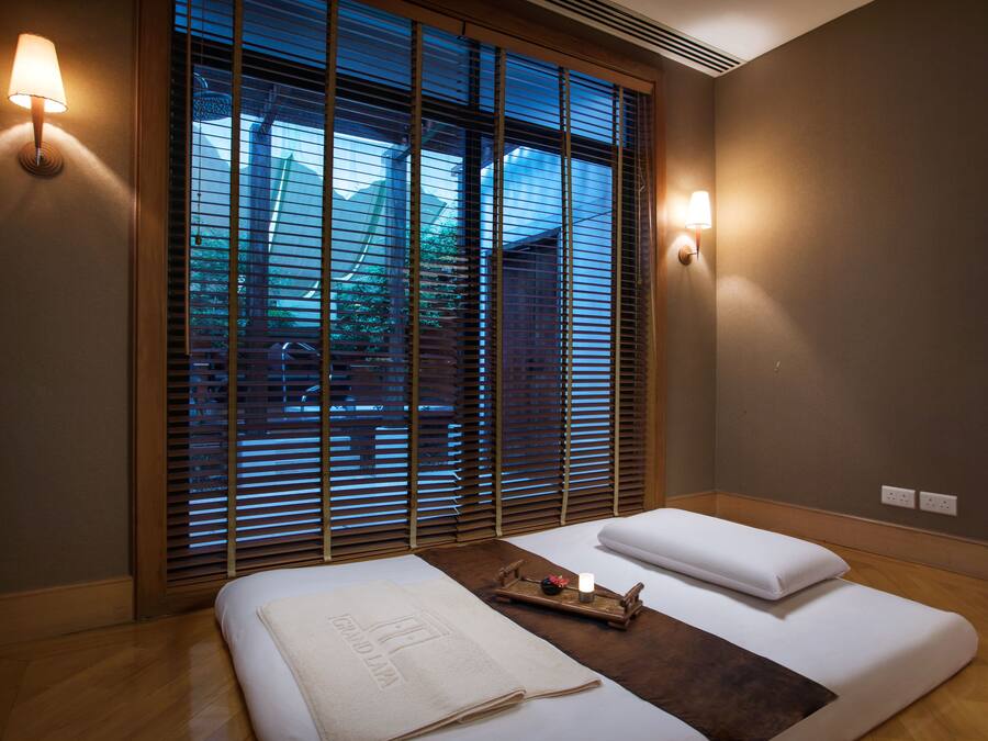 Habitación de hotel con cama, dos lámparas de noche, ventana con persianas y vista al exterior.