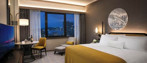 Una habitación de hotel con cama, escritorio, silla, televisor y ventana con vistas a la ciudad.