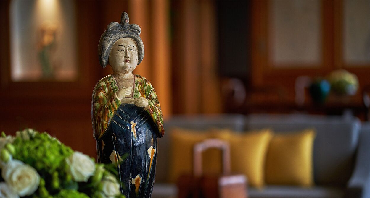 A statue of a woman in traditional attire, a sofa, and a vase with flowers.